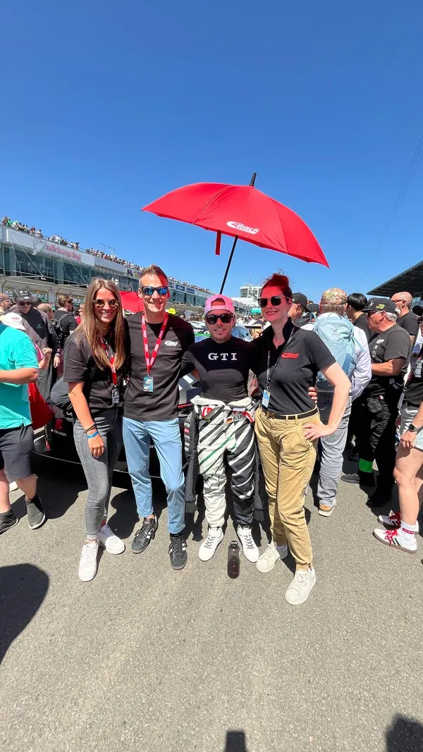 Wikivents team with Christopher, Elena, and event crew standing on the Nürburgring grid under a red Eibach umbrella